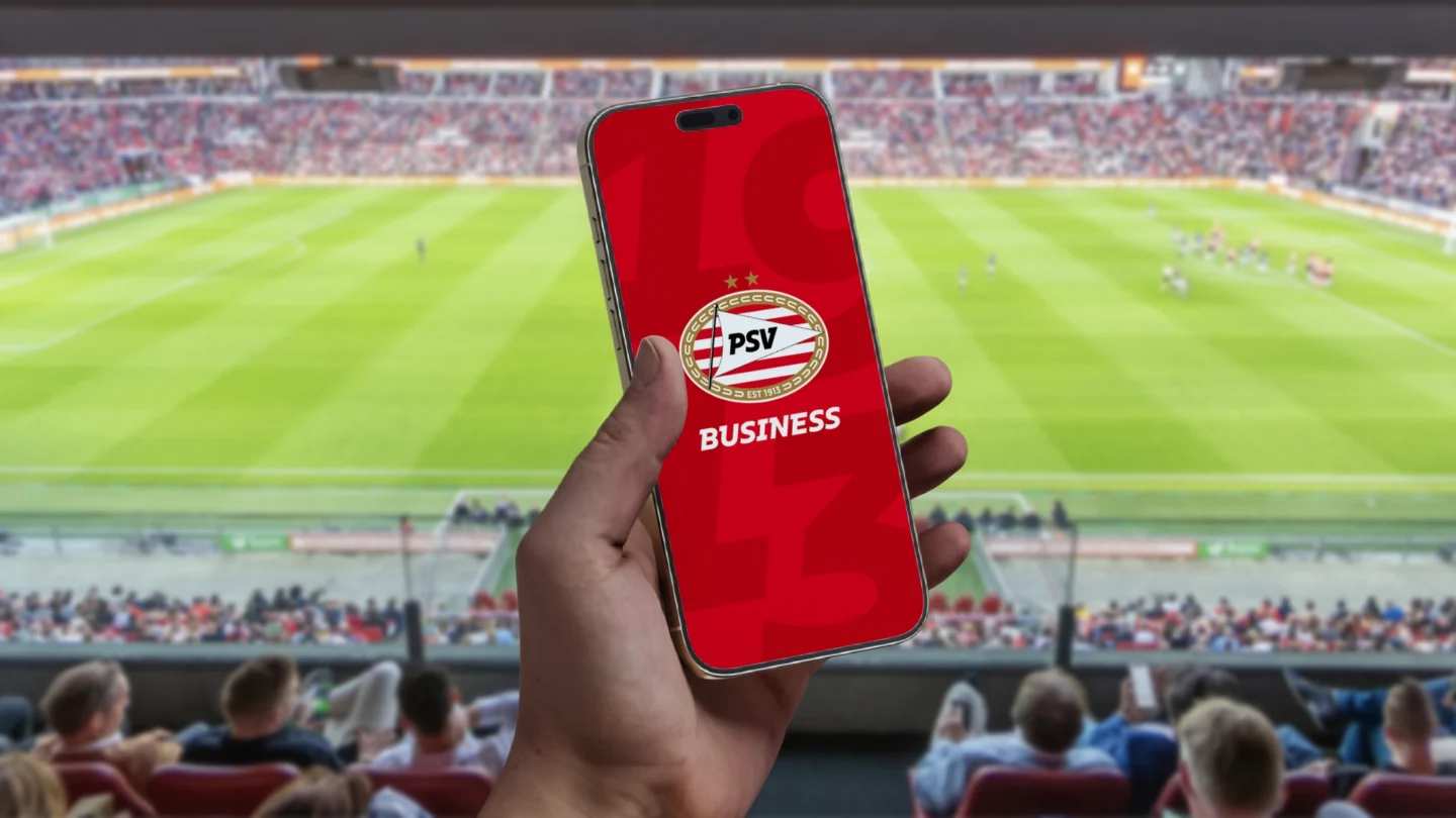 The PSV Business app in a hand with a football field in the background