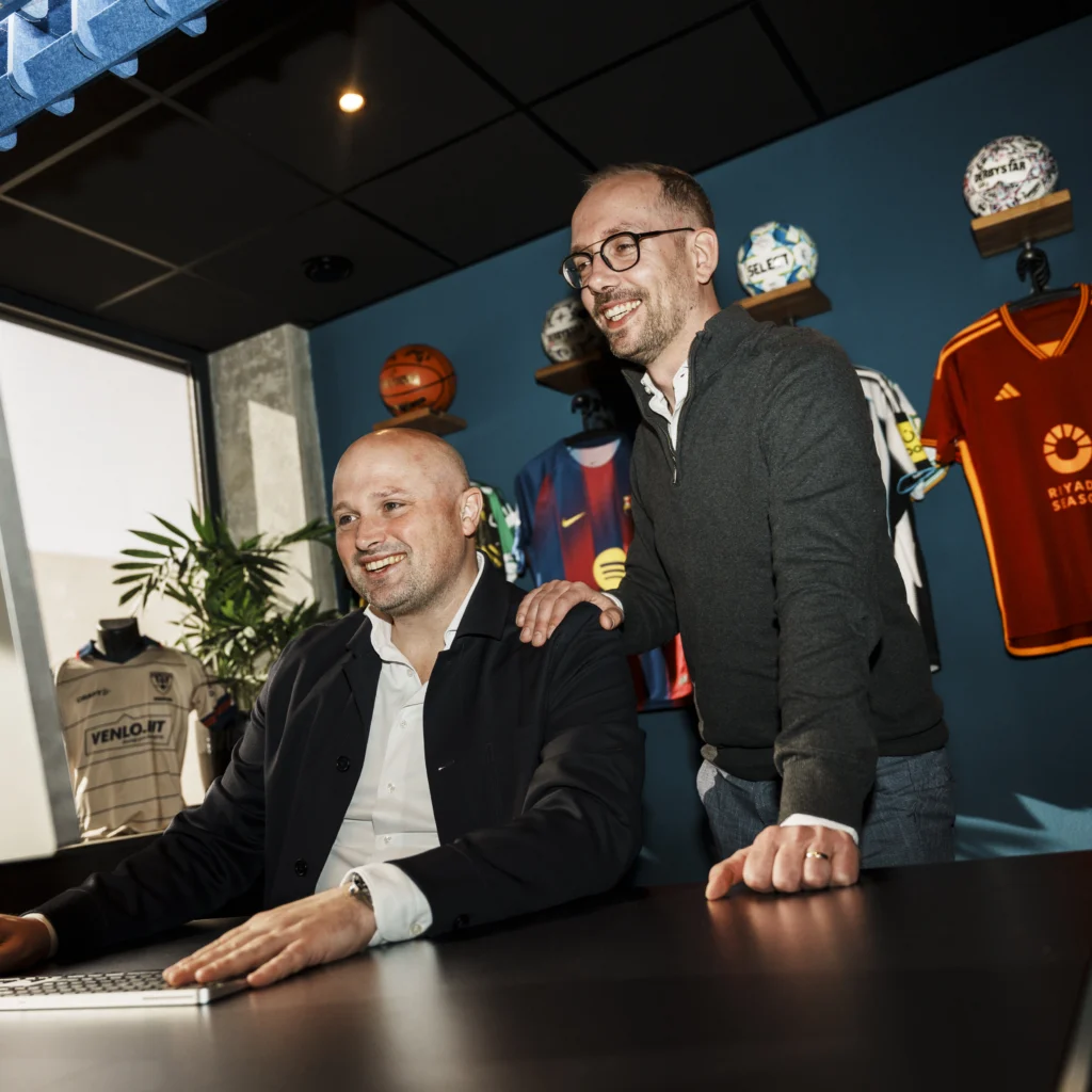 2 professional men smiling while looking at a computer together.