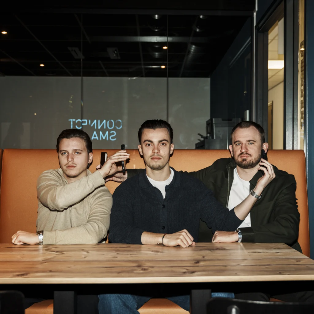 3 men holding a smartphone against each others ear which appear to be calling.